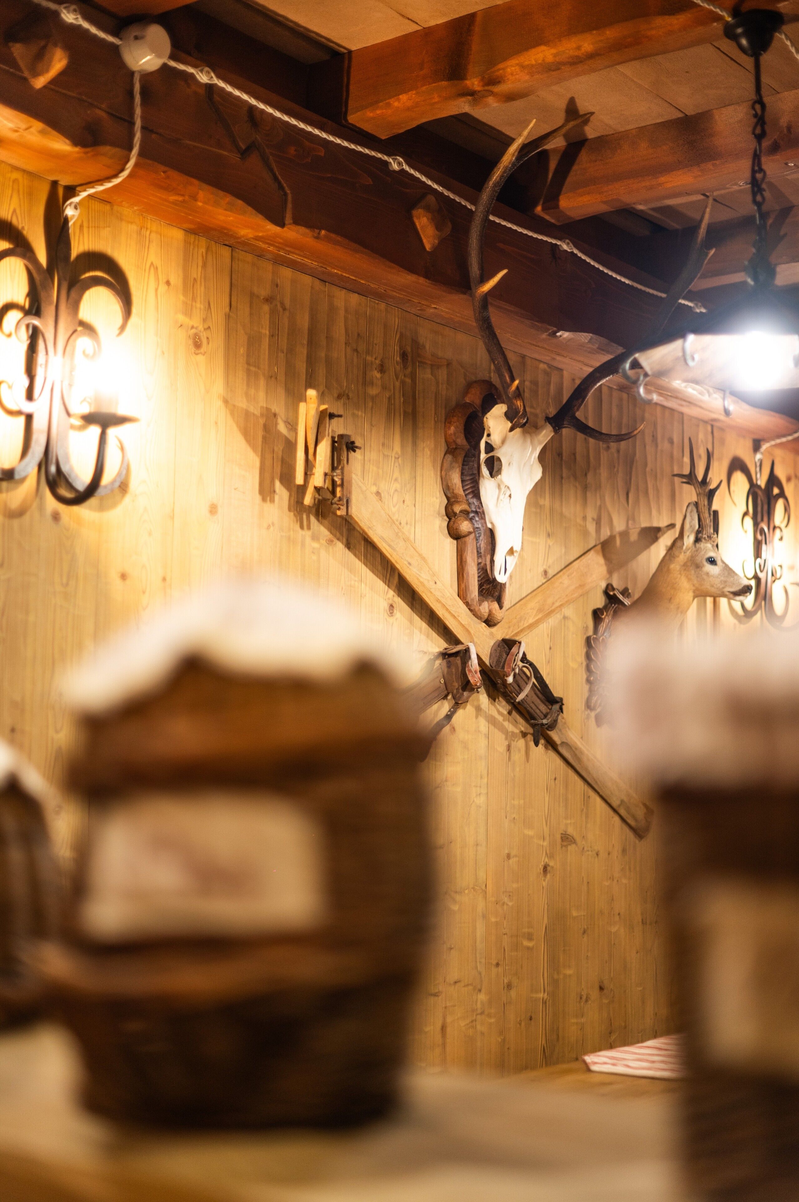 Interior rústico com paredes de madeira, crânios de animais pendurados e luminárias.