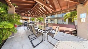 An outdoor patio with a covered seating area, including a table and chairs, surrounded by potted plants and a view of a building in the background. - Lovely 1BR1BA Condo  ~ Walk to Beach ~ Pool ~ BBQ (Oranjestad)