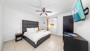 A hotel room with a bed, a nightstand, a TV, and a ceiling fan. - Lovely 1BR1BA Condo  ~ Walk to Beach ~ Pool ~ BBQ (Oranjestad)