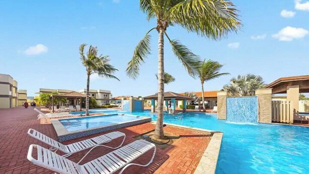 A swimming pool area with lounge chairs and palm trees. - Lovely 1BR1BA Condo  ~ Walk to Beach ~ Pool ~ BBQ (Oranjestad)