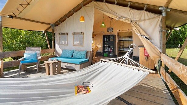 Un hébergement sous tente comprenant un hamac, une terrasse en bois et un canapé avec des coussins.