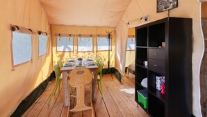L’intérieur d’une tente, avec une table à manger, des chaises, une bibliothèque et un luminaire au plafond.