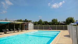 Une piscine avec des chaises longues, un petit bâtiment et un espace délimité par une clôture.