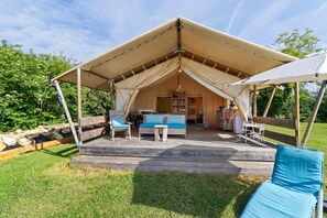 A tented accommodation with a wooden deck, seating area, and a kitchen visible inside.