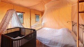 Ein Zeltraum mit Bett, einem Reisebettchen und einem Moskitonetz.