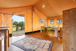 Una habitación con carpa, suelo de madera, una mesa con sillas y vistas al exterior.