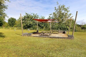 A picnic area with a wooden table and benches, surrounded by a wire fence and a red canopy.