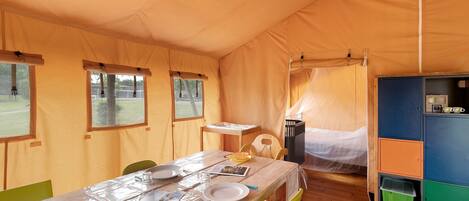 A tented accommodation with a dining area, a bed, and a small kitchenette.