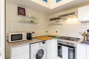 Una cocina compacta con microondas, lavadora, estufa, horno y estantes con utensilios de cocina.