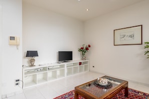 Una sala de estar moderna con televisor, mueble blanco para entretenimiento y una mesa de centro con objetos decorativos.