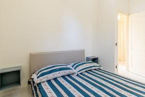 Un dormitorio con cama, dos mesitas de noche y una puerta que da a otra habitación.