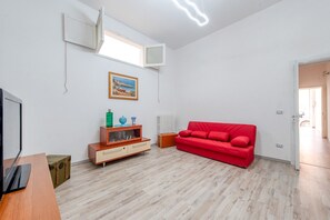 A room with a red sofa, a wooden cabinet, a television, and a window with an air conditioning unit.