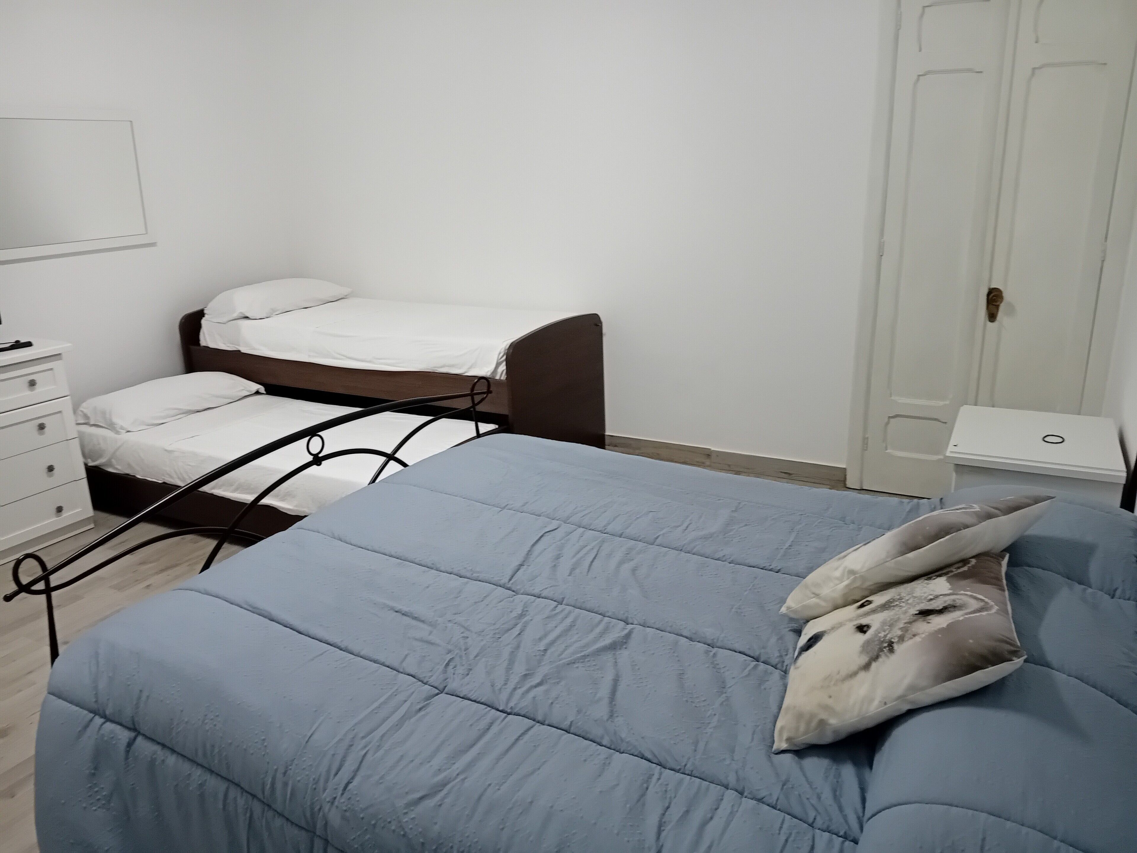 Een slaapkamer met een eenpersoonsbed, een kleiner bed, een dressoir en een kledingkast.