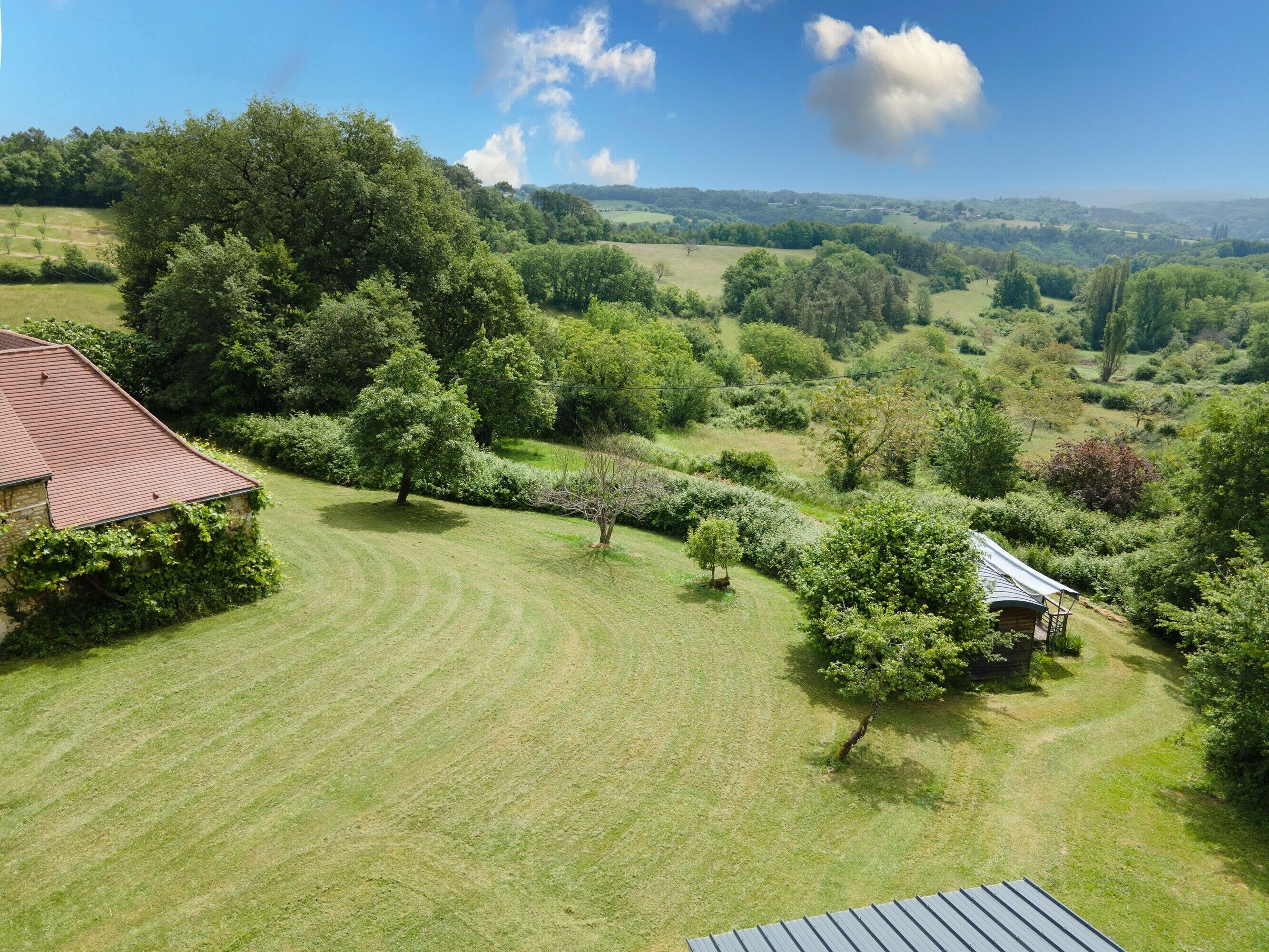 Ländliche Landschaft mit einem Haus, umgeben von üppigem Grün und sanften Hügeln.