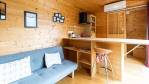 Interior de una cabaña de madera con sofá, mesa de comedor y pequeña cocina.
