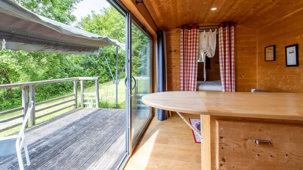 Interior de madera con un ventanal grande, una mesa y vistas a follaje exterior.