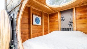 Ein gemütliches Schlafzimmer in einer Holzhütte mit einem Bett, einem runden Dachfenster und einem gerahmten Bild an der Wand.
