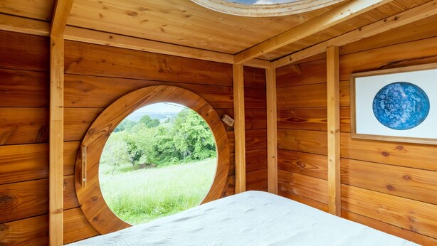 Ein Zimmer aus Holz mit einem Rundfenster, einem Bett und einem gerahmten Globus.