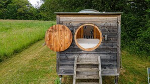 Eine Holzhütte mit zwei Rundfenstern und einer Leiter zum Bett.
