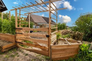 Puinen portti, jonka yläosassa on pergola, kukkapenkki kasveineen ja taustalla näkyvä talo.