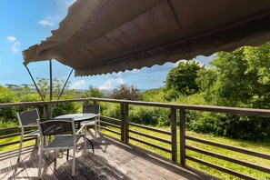 A wooden deck with a table and chairs under a canopy, surrounded by lush greenery and a view of distant hills. - Escape to Domaine de la Salamandre: Nature, Serenity & Sustainable Living (Auriac-du-Périgord)