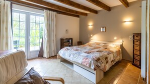 Une chambre à coucher comprenant un lit, une chaise, un bureau, une fenêtre avec des rideaux et une étagère fixée au mur.