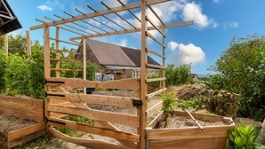 Une porte en bois surmontée d’une pergola, un parterre fleuri et une maison en arrière-plan.