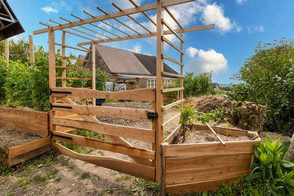 Ein hölzernes Tor mit einer Pergola, ein Gartenbeet mit Pflanzen und ein Haus im Hintergrund.