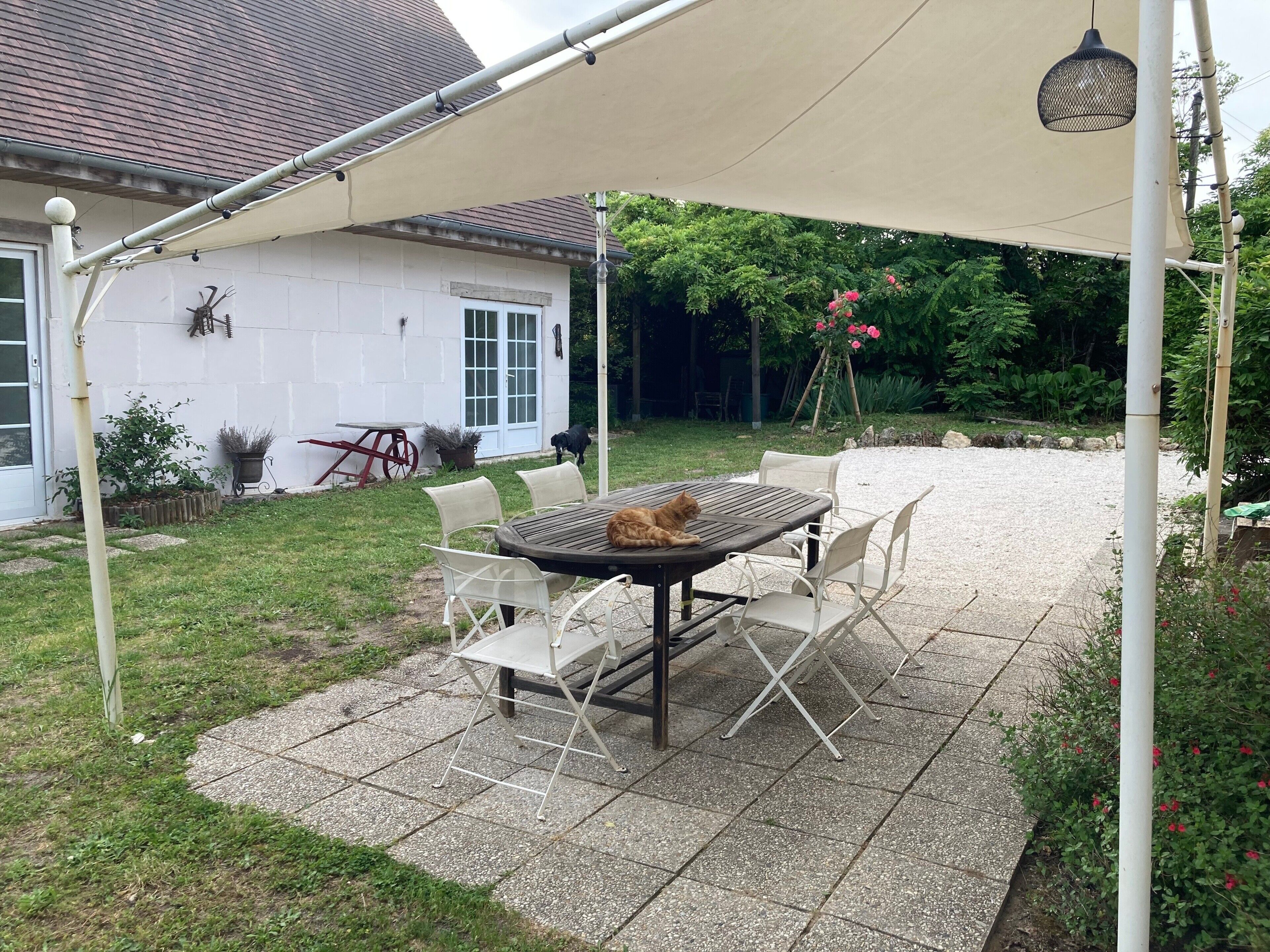 Un patio con una mesa y sillas, un área cubierta y una casa al fondo.