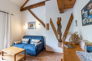 Uma sala de estar com um sofá azul, vigas de madeira, uma mesa pequena e um quadro pendurado na parede.