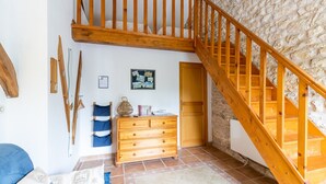 Una habitación con escalera de madera, cómoda de madera, cama con ropa de cama azul y pared de piedra.