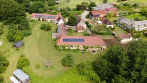 Vista aérea de una propiedad rural con varias construcciones, incluyendo una casa con paneles solares, rodeada de exuberante vegetación y campos.