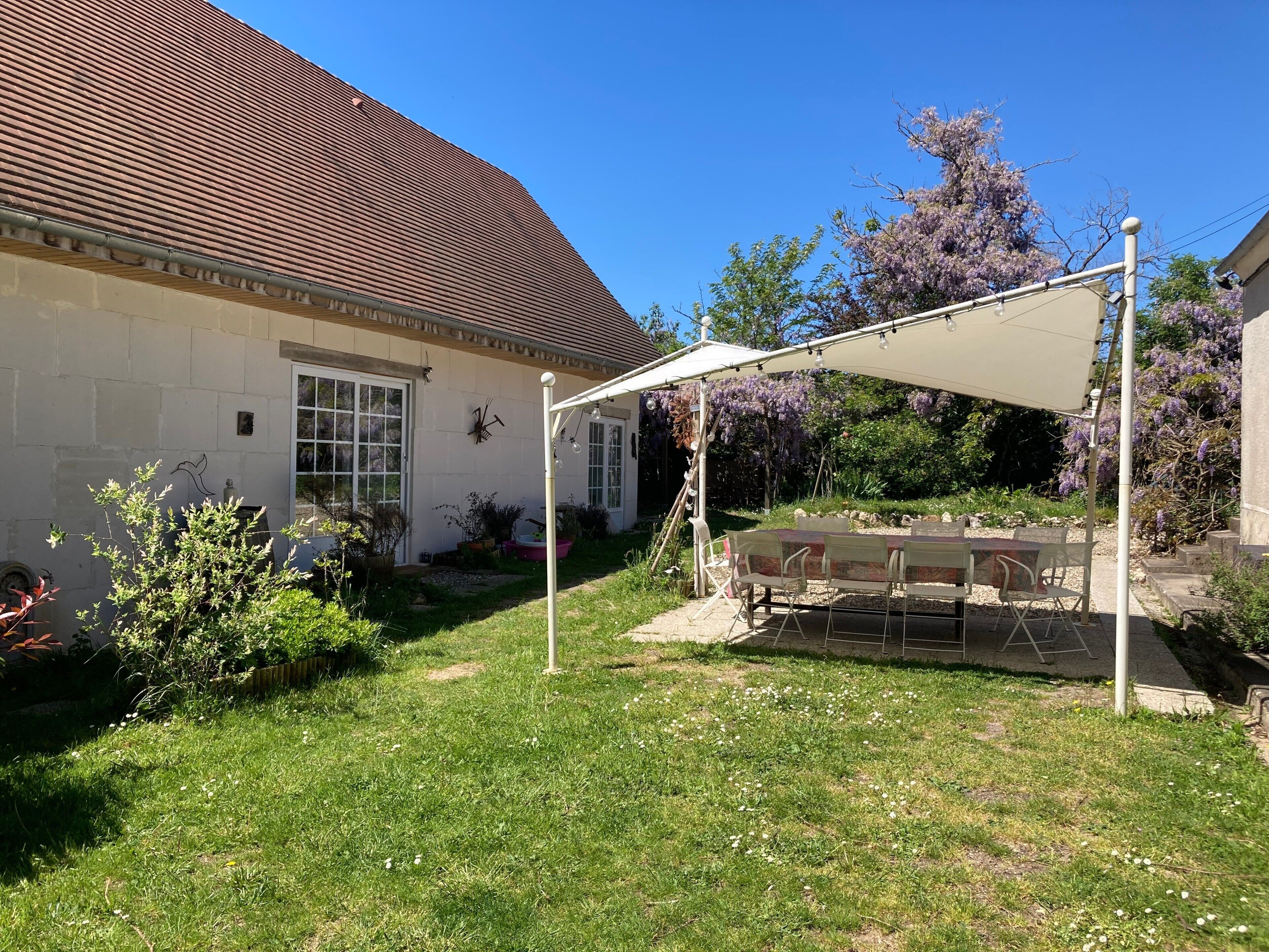 Een huis met een patio, een overdekte zithoek en een tuin met diverse planten.