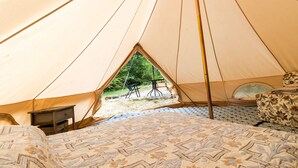 A tent with a bed, a small table, and a view of a tree outside.