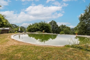 Um lago circular com área gramada e árvores ao fundo.