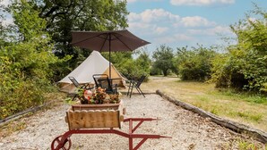 A tent with a table and chairs, a wooden cart with plants, and a large umbrella.