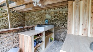 A rustic kitchen with a stone wall, wooden beams, a white sink, and a wooden cabinet.