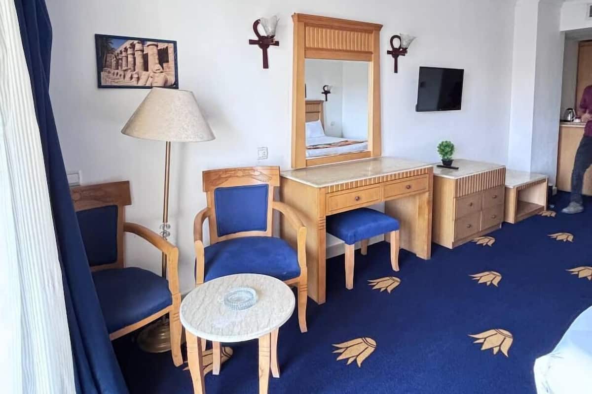 Camera d'albergo con tappeto blu, mobili in legno, una scrivania con uno specchio, una lampada e una televisione.