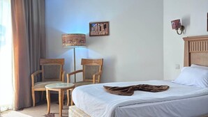 Une chambre d’hôtel comprenant un lit, deux chaises, une petite table, une lampe et un luminaire fixé au mur.