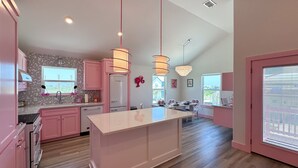 A modern kitchen with pink cabinets, a central island, pendant lights, and a chandelier. - Barbie Themed, Pet Friendly, Parking for 4 Vehicles (Port Aransas)