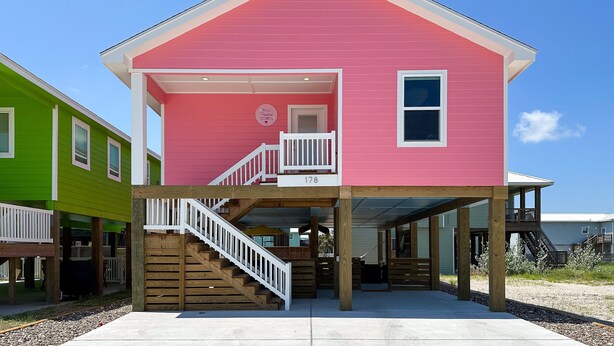 A pink house with a wooden deck and a staircase leading to a porch. - Barbie Themed, Pet Friendly, Parking for 4 Vehicles (Port Aransas)