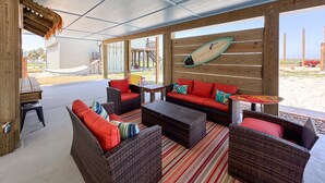 An outdoor patio with wicker furniture, a surfboard, and a view of the beach. - Barbie Themed, Pet Friendly, Parking for 4 Vehicles (Port Aransas)