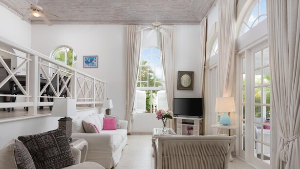 A spacious living area with a white sofa, a wicker chair, a TV, and a small table with a lamp.