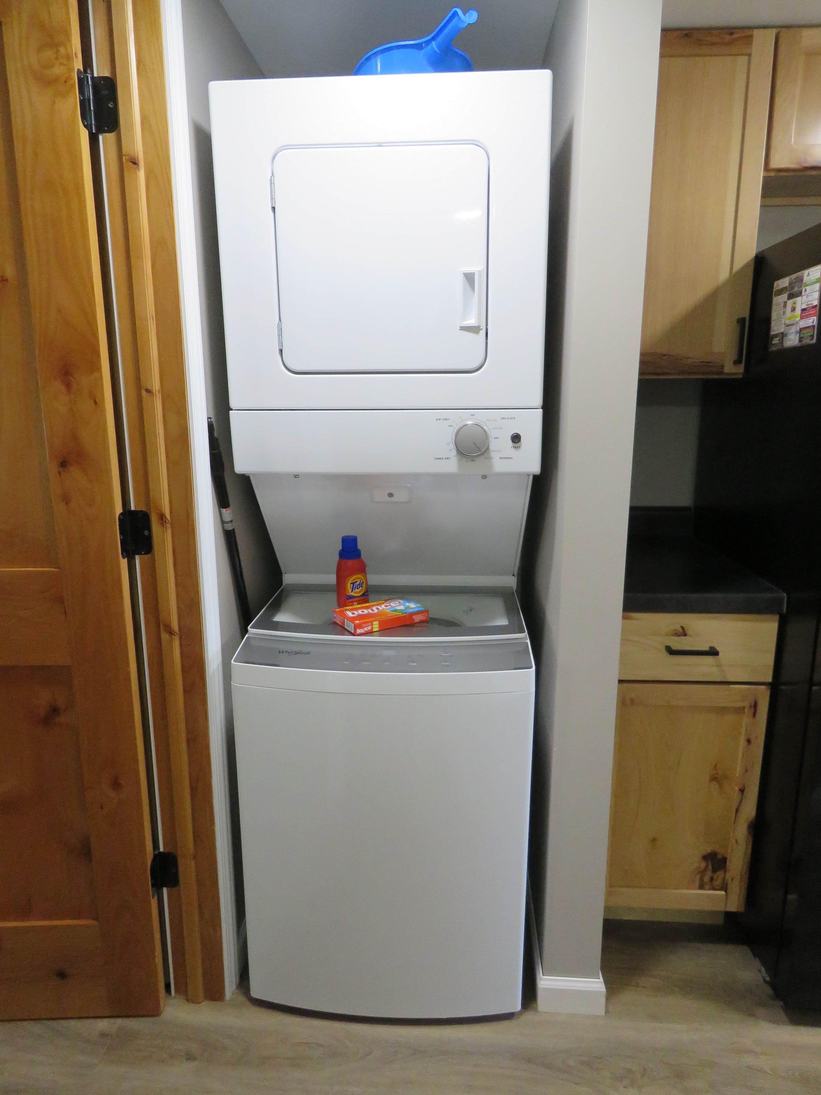 A compact washer and dryer unit with a control panel, a bottle of detergent, and a box of fabric softener on the top.