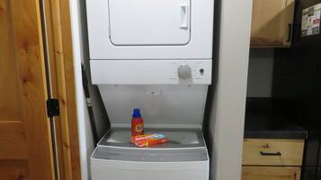 A compact washer and dryer unit with a control panel, a bottle of detergent, and a box of fabric softener on the top.