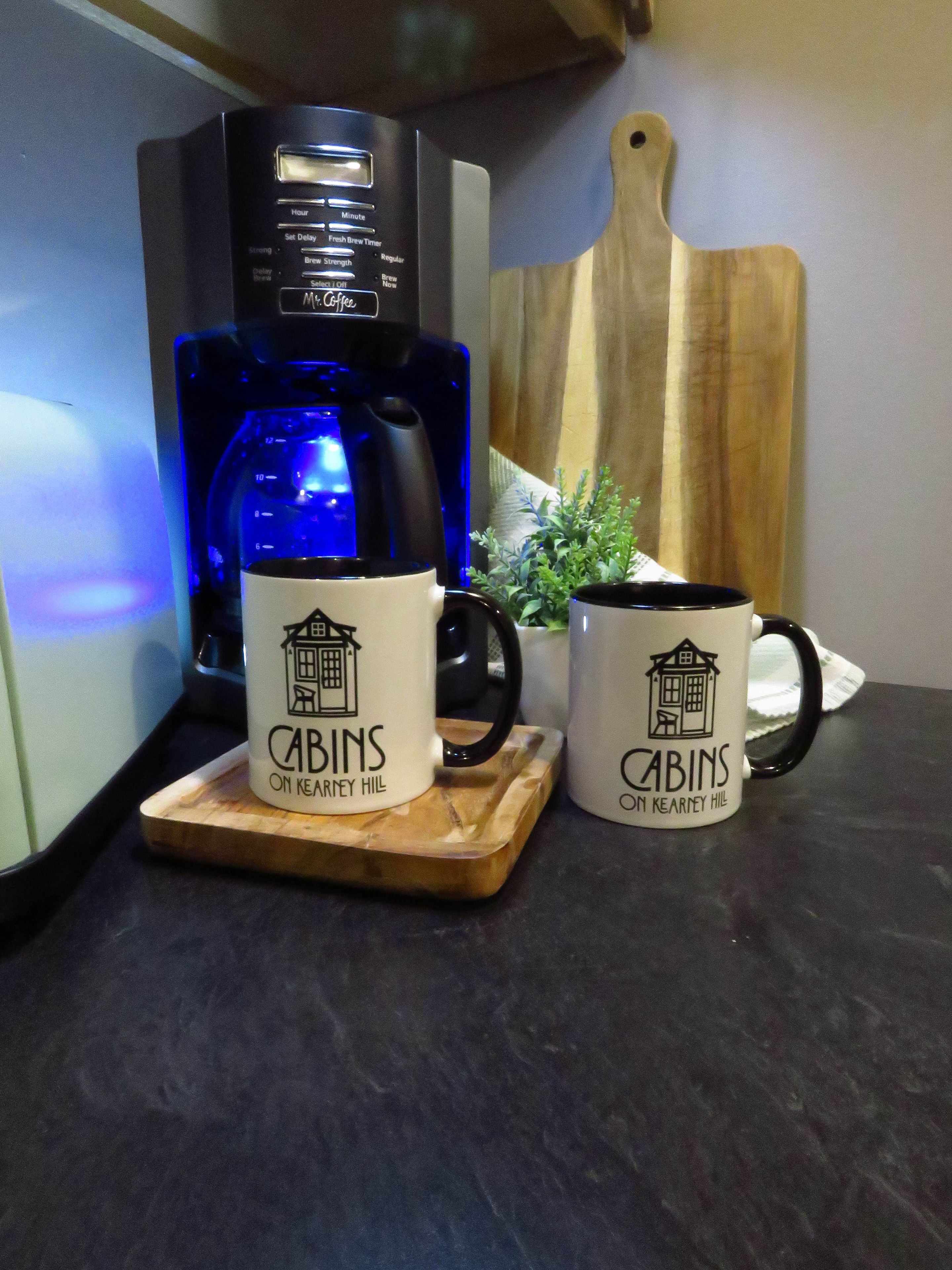 En kaffebryggare med en digital display och en skärbräda i trä med muggar på.