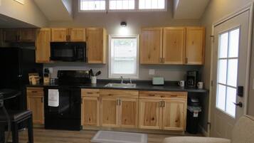 A compact kitchen with wooden cabinets, a black refrigerator, and a microwave.