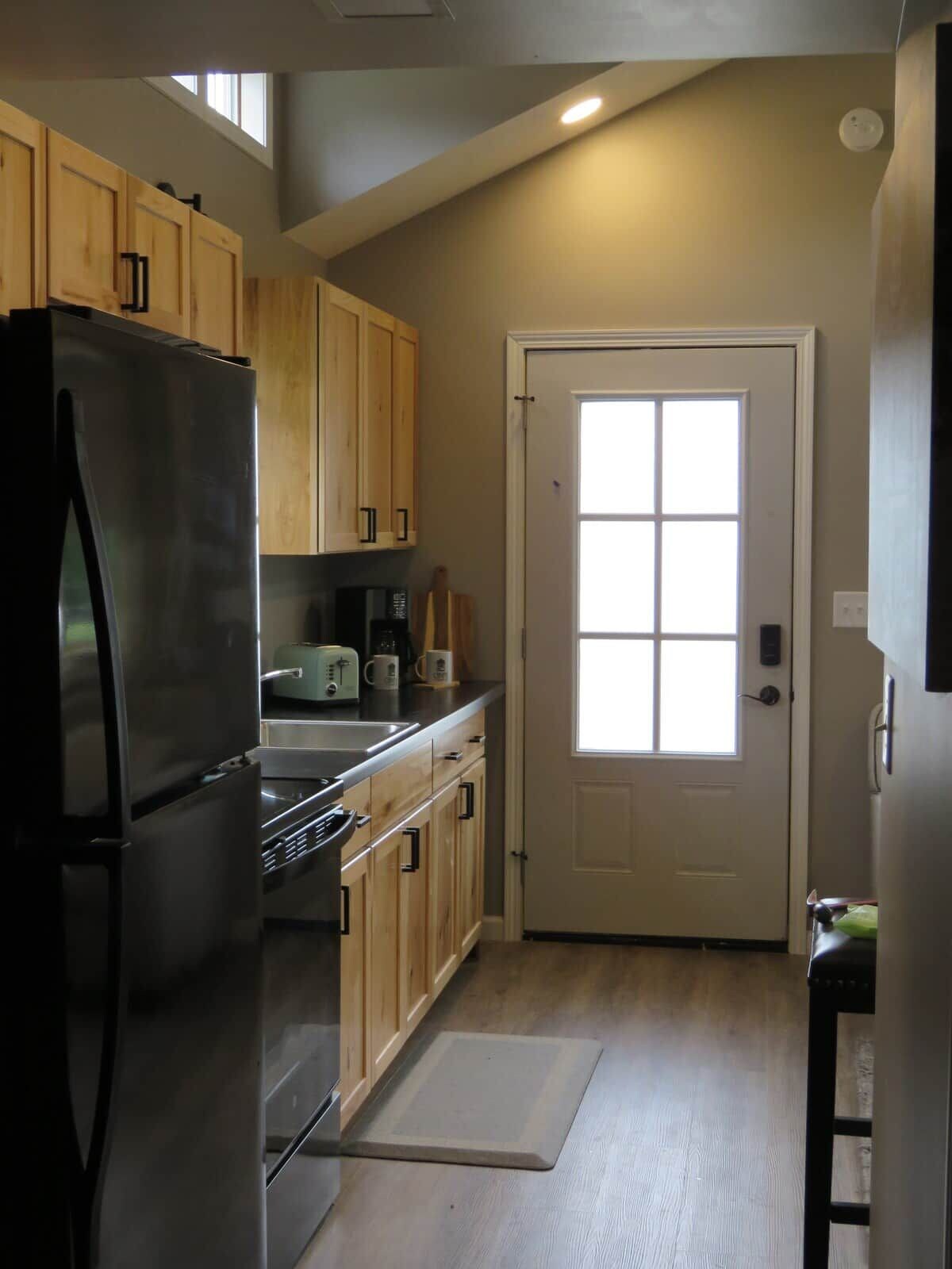 A kitchen with wooden cabinets, a stainless steel refrigerator, a microwave, and a window above the door.