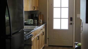 A kitchen with wooden cabinets, a stainless steel refrigerator, a microwave, and a window above the door.