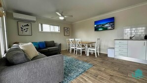 A modern living room with a grey sofa, a dining table with white chairs, a kitchen area with white cabinets, and a ceiling fan. - 2B at Swansea - cosy cottage, outdoor pet friendly (Swansea)